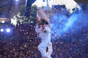 Hombre con traje blanco, pañuelo rojo, sombrero de hojas y estructura pirotécnica con chispas en la cabeza, humo azul y multitud de fondo