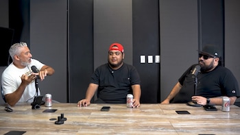 Tres hombres sentados frente a una mesa con micrófonos, latas de refresco y teléfonos móviles ante una pared oscura