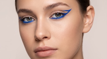 Primer plano del rostro de una mujer con ojos claros y un delineado azul eléctrico en los párpados y la línea de agua.