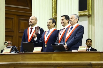 Cuatro hombres con traje oscuro y bandas ceremoniales bicolores posan detrás de un podio de madera. Uno sostiene un libro con la tapa que dice "Constitución Política del Perú 1993"