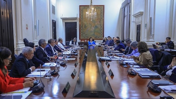 Autoridades gubernamentales sentadas alrededor de una larga mesa de madera en una sala de reuniones con una araña de cristal