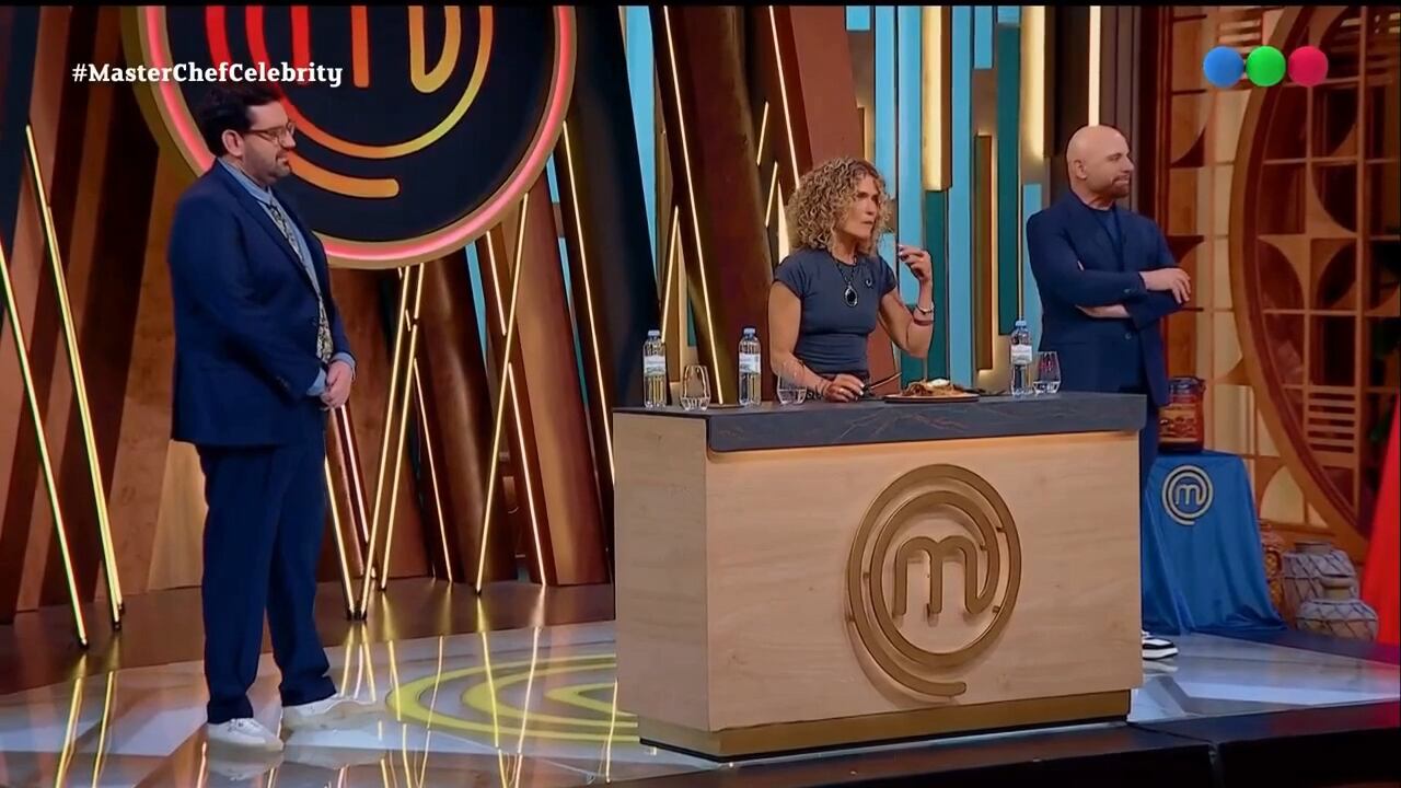Los miembros del jurado de MasterChef Celebrity escuchan las explicaciones y evalúan una preparación gastronómica frente al estrado del estudio de televisión.