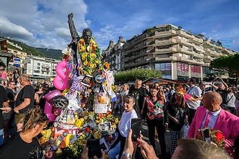 Una estatua de bronce con un brazo en alto está cubierta de flores, guirnaldas y globos mientras varias personas la fotografían