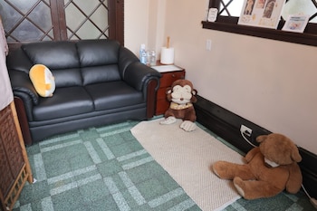 Un sofá de cuero negro con un cojín de peluche amarillo. Junto a él, una mesa auxiliar de madera, un rollo de papel y dos peluches de mono y oso sobre una alfombra