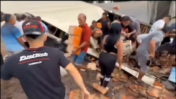 Vista de personas cargando cajas y artículos desde un camión volcado en un camino de tierra o escombros en una escena caótica