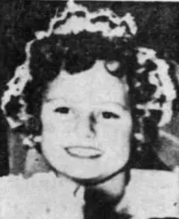 Fotografía en blanco y negro de una niña sonriente con cabello oscuro y rizado que lleva una tira de encaje sobre la cabeza