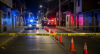 Una calle urbana de Irapuato, Guanajuato, de noche, acordonada con cinta amarilla de policía. Patrullas con luces rojas y azules y conos naranjas son visibles.