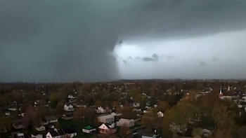 Vista aérea de un área residencial con casas y árboles bajo un cielo oscuro. Un relámpago brillante es visible en las nubes de una tormenta