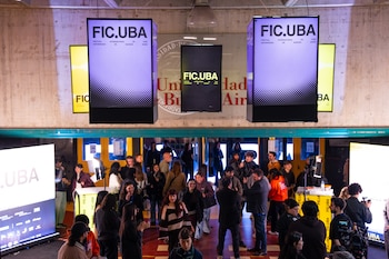 Personas en un salón iluminado por pantallas colgantes con la inscripción FIC.UBA y el emblema de la Universidad de Buenos Aires al fondo