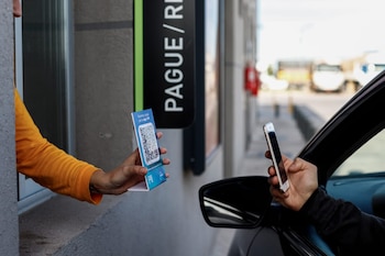 Dos manos interactuando; una sostiene un código QR de YPF y la otra un smartphone para escanearlo, en un entorno de pago exterior