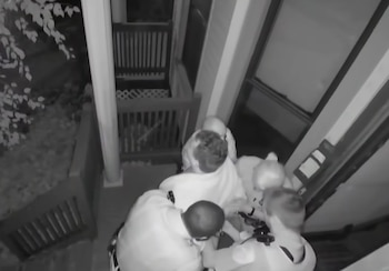 Imagen en blanco y negro de cámara de seguridad donde varios policías sujetan a un hombre en la entrada de una casa
