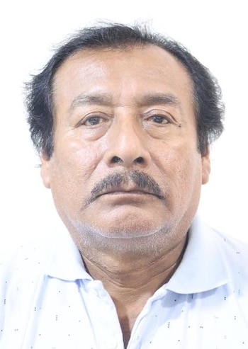 Retrato en plano medio de un hombre con bigote, cabello oscuro y camisa polo clara sobre un fondo blanco