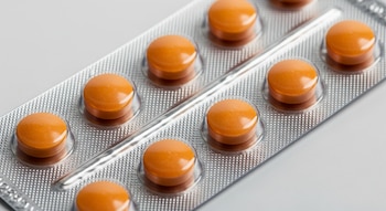 Primer plano de un blíster plateado que contiene pastillas de bisacodilo redondas y de color anaranjado, alineadas ordenadamente sobre un fondo blanco.