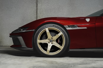 Automóvil deportivo rojo, vista lateral del frontal. Rueda dorada de cinco radios, neumático Michelin, pinza de freno Ferrari, emblema de la marca