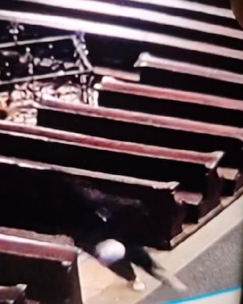 Imagen borrosa de vigilancia muestra a una persona vestida de oscuro, con un objeto blanco, entre estructuras con líneas horizontales