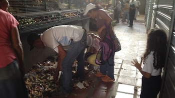 Una niña observa cómo un grupo de adultos busca alimentos entre la basura. (Gentileza El Nacional)