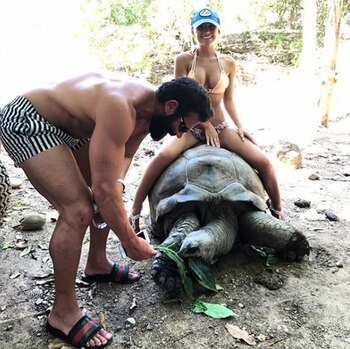 Sofía Bevarly sentada sobre una tortuga de 100 años, mientras “El Rey de Instagram” le da de comer