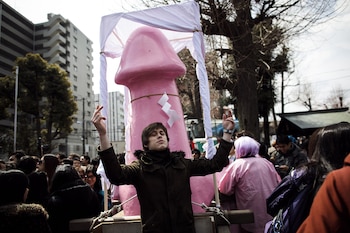 Un hombre posa al lado de un gran monumento fálico durante el Festival de Kanamara, anual, en Kawasaki. el 2 de abril de 2017 (AFP)