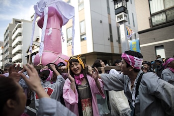 Una mujer posa al lado del monumento fálico que cargan durante el Festival del Pene de Acero en Kawasaki (AFP)