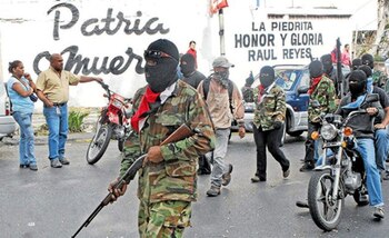 Un miembro de los colectivos chavistas armado y de fondo el mural de La Piedrita en honor a Raúl Reyes, fallecido jefe guerrillero de las FARC