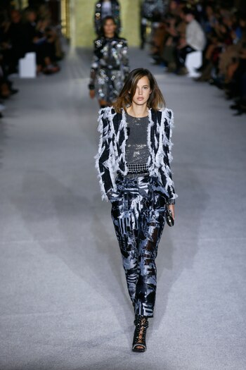 Chaquetas con hombreras combinadas con plumas blancas, pantalones en taftan con diseño abstracto y booties en charol negro con tientos