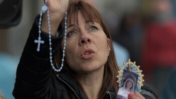 Una mujer sostiene un rosario y la imagen de la Virgen María mientras reza mirando al cielo