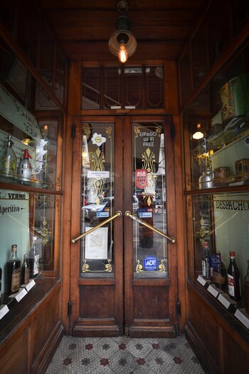 Sus puertas de madera con manijas de acero. Decoraciones de botellones con años de antigüedad y grandes historias detrás. Sigue manteniendo la fachada, sus ventanales y puertas originales