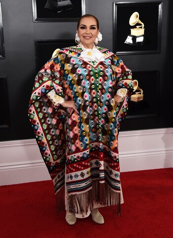 Aida Cuevas eligió para los Grammy un poncho con rombos multicolor y flecos. La cantante y actriz llevó debajo una camisa blanca con detalles bordados en dorado y plateado con maxi botones y moños en el cuello. Como gran accesorio, flores en el peinado y argollas doradas