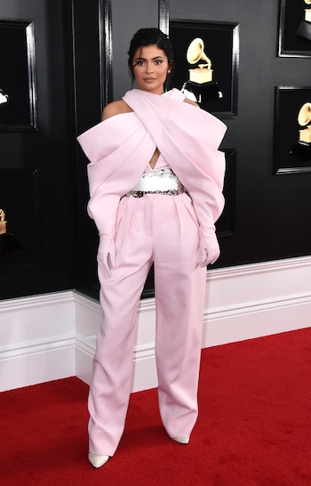 Kylie Jenner llegó a la alfombra roja de los Grammy con un look oversized en rosa bebé con mangas cruzadas y guantes. Completó el look con stilettos en punta blancos y cinturón blanco