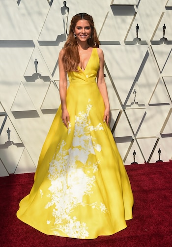 Maria Menounos también eligió el color amarillo para la alfombra roja, Con un gran escote V y con estampado floral en blanco. Cabello suelto y pequeños aros