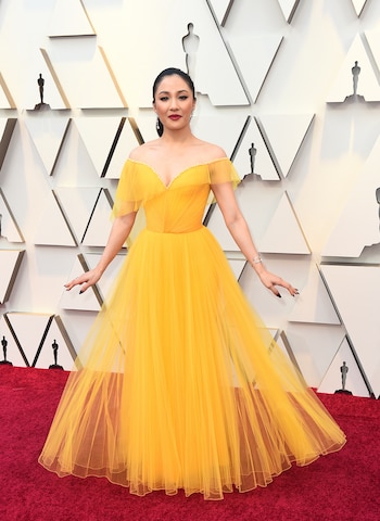 Constance Wu apostó al color amarillo by Versace. Un vestido escote corazón y corte en la cintura drapeado y de tul. Brazalete de brillantes, anillos y aros colgantes. Cabello recogido y maquillaje con labios colorados