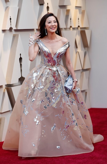 Michelle Yeoh impactó con un vestido voluptuoso de organza bordado con paillettes plateados by Elie Saab. Completó el look con clutch de raso. Un brazalete de flores, reloj en oro rosa y aros colgantes