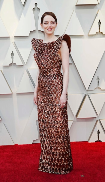Emma Stone sorprendió con su vestido de paillettes en bronce de rombos y hombros armados. Completó el look con un anillo y pequeños aros. Su beauty look, smokey eye en marrones y labios nude