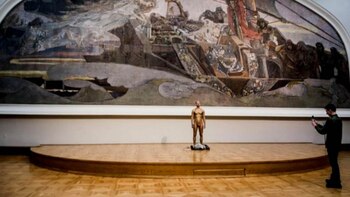 El hombre desnudo y pintado de dorado posa frente a una obra del museo