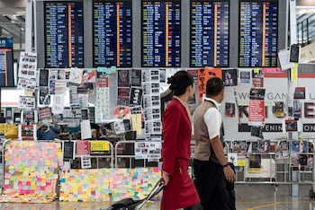 El 13 de agosto de 2019, al día siguiente de que el aeropuerto de Hong Kong cerrara sus puertas debido a las protestas a favor de la democracia, dos azafatas pasan por delante de un tablero de anuncios eléctrico cubierto de carteles (Foto de Philip FONG / AFP)