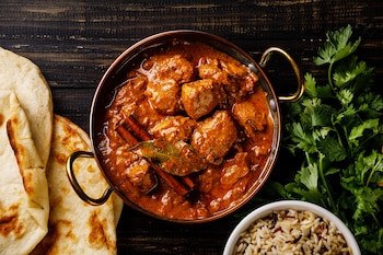 Sumerja el pan naan en el pollo tikka masala, una comida india clásica con especias y una cremosa salsa de tomate