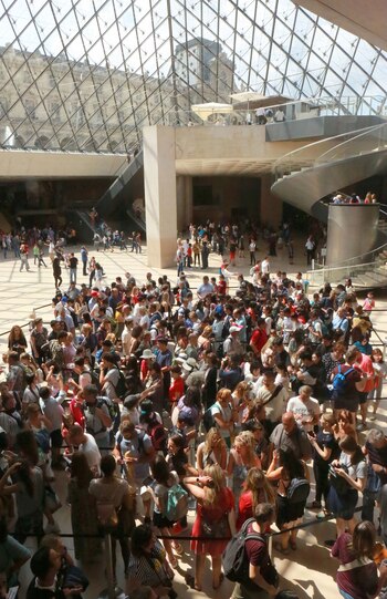 Una multitud hacía fila bajo la pirámide de cristal del Louvre en espera de su turno frente a la Mona Lisa. Los visitantes deben tomar tres ascensores para llegar a la pintura (Owen Franken para The New York Times)