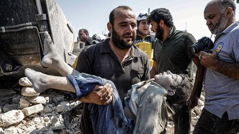 Un sirio carga el cuerpo de un niño fallecido en un bombardeo del régimen en Deir Sharqi (Photo by Abdullah Hammam / AFP)